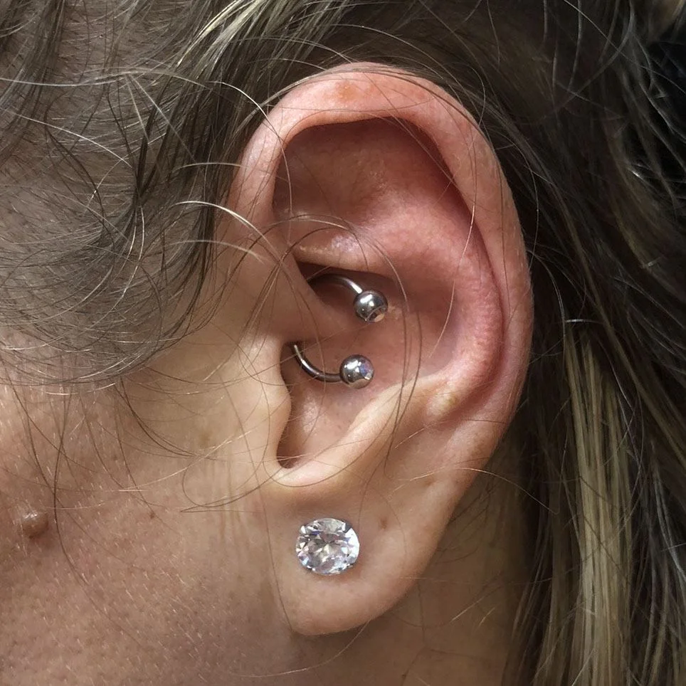 Ezüst színű daith piercing patkóval és köves fülbevalóval Daith piercing ezüst színű patkó ékszerrel és alsó köves fülbevalóval női fülben